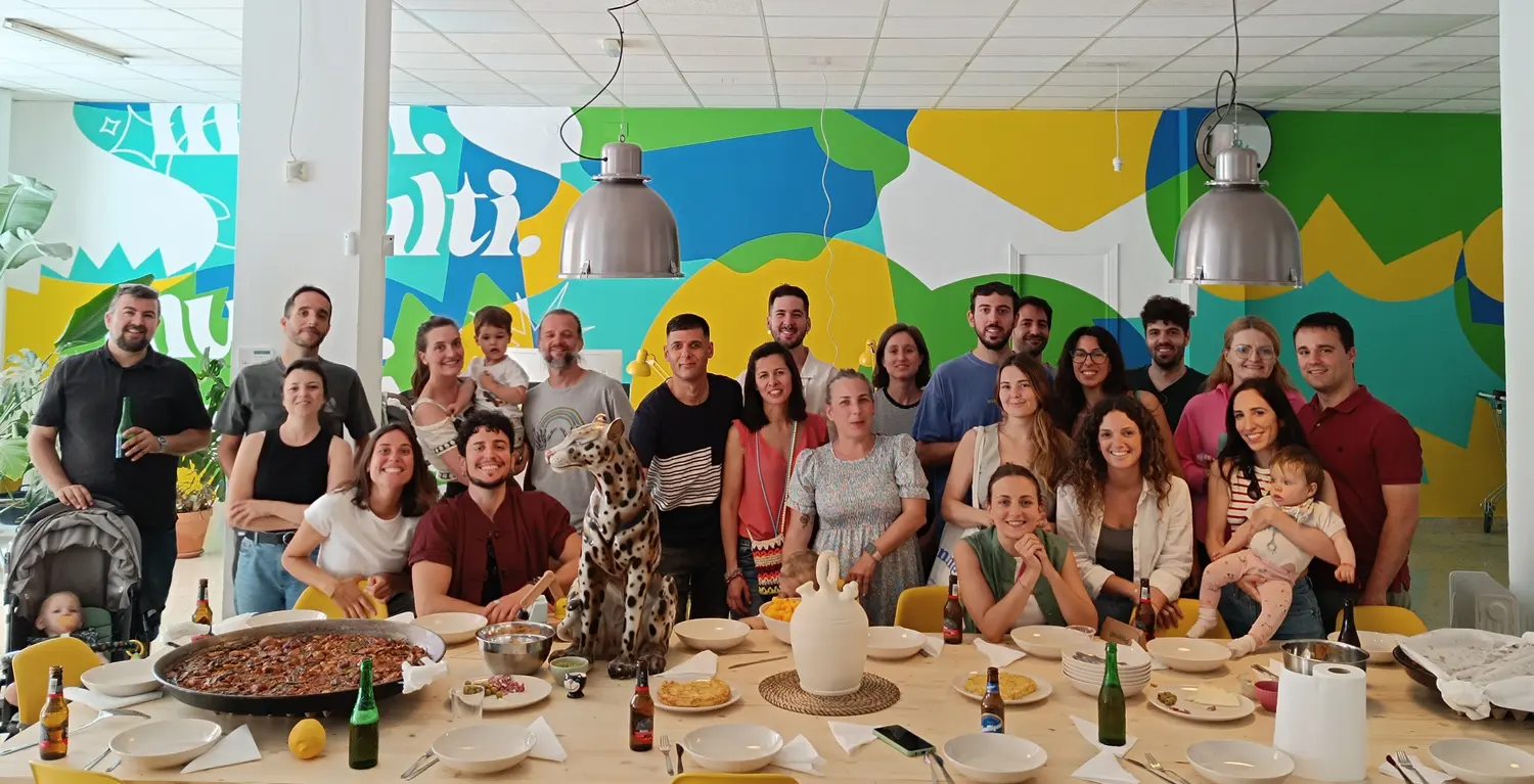 La comunidad de Multiprecio reunida alrededor de una mesa larga, frente al mural